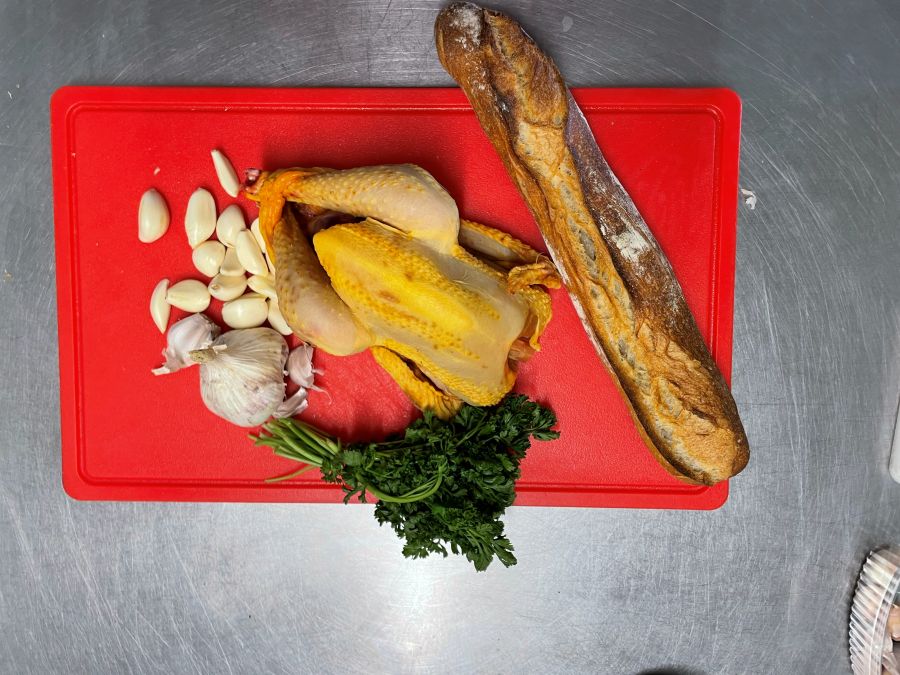 Poulet fermier cru avec ail, persil et pain sur une planche rouge